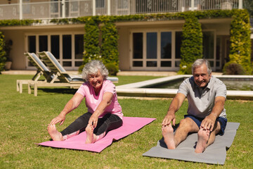 Portrait of senior caucasian couple practicing yoga, stretching in sunny garden