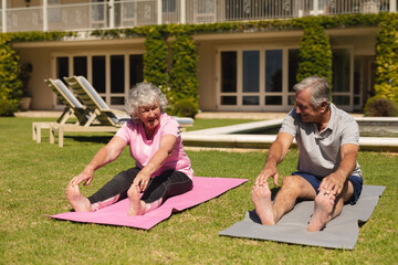 Senior caucasian couple practicing yoga, stretching in sunny garden