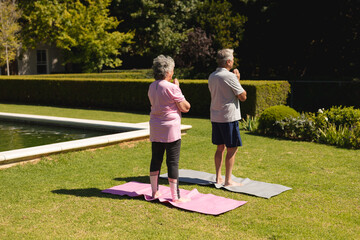Naklejka premium Senior caucasian couple practicing yoga, meditating in sunny garden