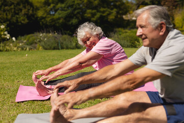 Senior caucasian couple practicing yoga, stretching in sunny garden