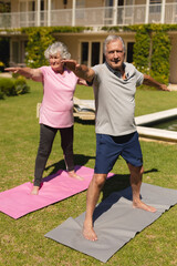 Naklejka premium Senior caucasian couple practicing yoga, stretching in sunny garden