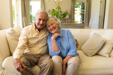 Portrait of senior caucasian couple sitting on sofa embracing and smiling