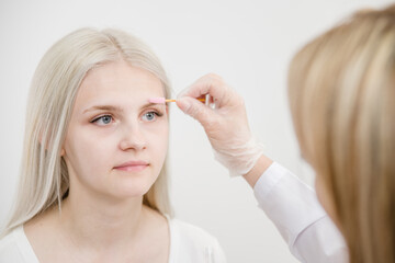 Cosmetologist combs  eyebrows before permanent make-up in beauty salon