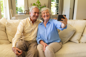 Senior caucasian couple sitting on sofa having video call using smartphone