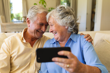 Senior caucasian couple sitting on sofa having video call using smartphone