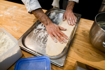 view of male chef's hands who adjusts the dough on the baking sheet.