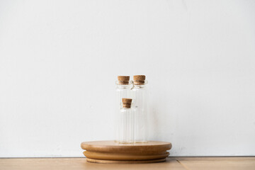 Three glass bottles with cork stopper on wooden podium with white wall background. Essential oil refilling store. Mockup template. 