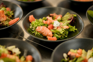 selective focus of black bowl of salmon salad with arugula and other greens