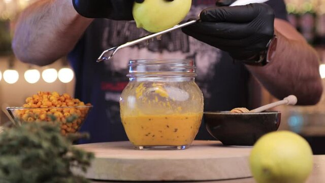 a man scrapes lemon peel in to a jar with sea buckthorn