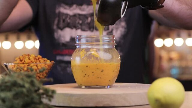a man pours honey into a jar of sea buckthorn