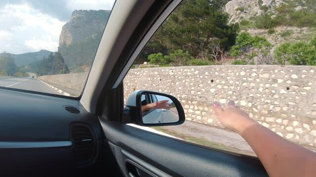 Female traveler playing waving hand automobile window enjoying car trip at mountain landscape