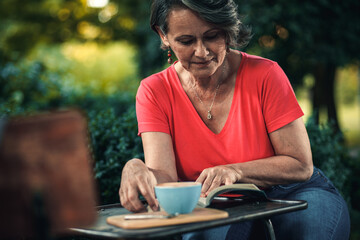 Senior woman reading book in outdoor coffee shop.