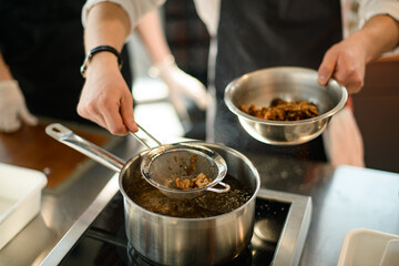 male chef's hand pulls nuts from a boiling pot using a sieve