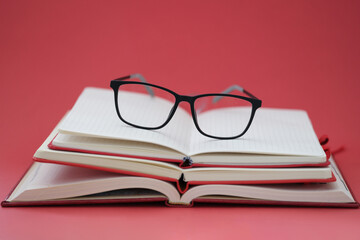 Glasses for sight lying on pile of notebooks on red background closeup