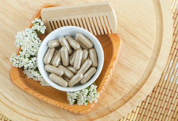 Small white bowl with food supplement capsules, wooden hair brush and yarrow flowers. Natural...