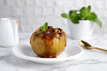 Delicious baked apple with nuts, caramel and mint served on white marble table