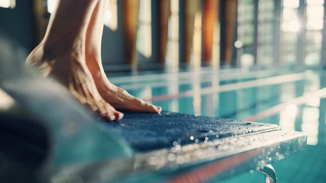 Olympic Swimming Pool: Professional Swimmer Steps on Starting Block. Overcoming Fear, Determined Athlete Ready to Set New Record on a Championship. Stylish Cinematic Focus on Legs. Bokeh Close-up