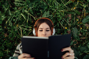 Woman in headphones reading book on grass