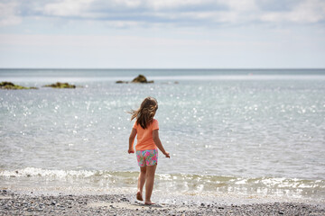 Fototapeta na wymiar 5-year-old girl in summer clothes in front of the ocean looking at the horizon. Summer and vacation concept