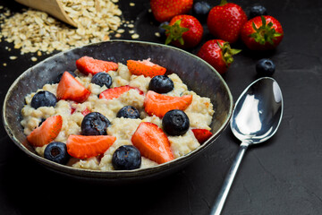 The concept of a healthy breakfast of oatmeal with strawberries and blueberries