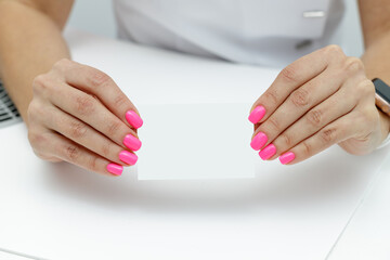 Obraz premium Female hands with pink manicure holding empty visit card.