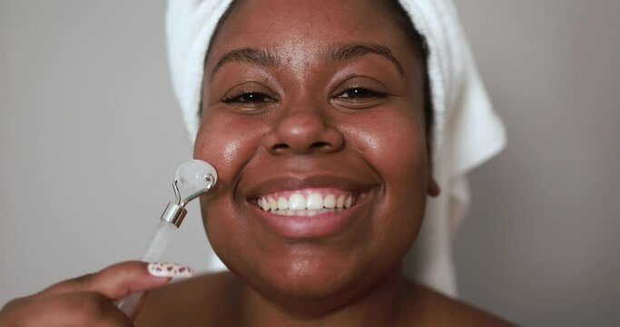 African young woman using rose quartz jade roller for her face - Beauty treatment and body care concept