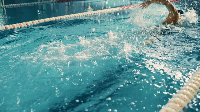 Male Swimmer Swimming in Olympic Pool. Professional Athlete Performing at Championship, using Front Crawl, Freestyle. Determination to Win. High Angle Cinematic Rear Tracking Slow Motion