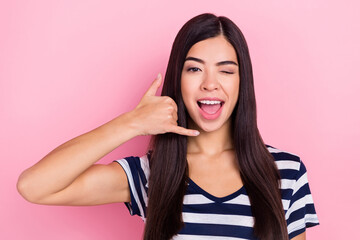 Photo of funny sweet young lady dressed striped clothes smiling showing phone gesture isolated pink...