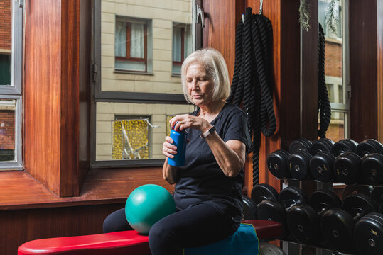 Elderly sportswoman opening bottle of water during training in gym