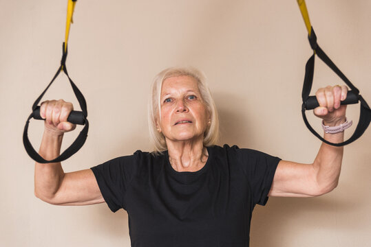 Senior sportswoman exercising with straps on light background