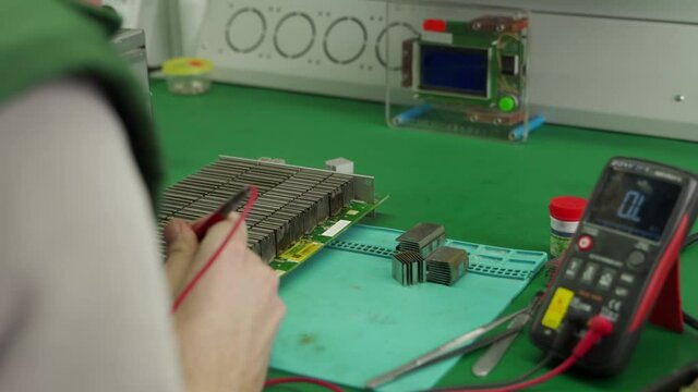 Technician testing the circuit board with multimeter. Engineer repairing bitcoin ASIC miner PCB. Reflowing chip contacts and cooler replacement.