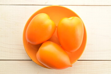 Three juicy yellow plum tomatoes on a ceramic saucer, on a wooden table, close-up, top view.