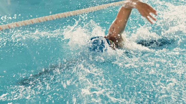 Male Swimmer Swimming in Olympic Pool. Professional Athlete Performing at Championship, using Front Crawl, Freestyle. Determination and Best Effort to Win. High Angle Cinematic Back Tracking