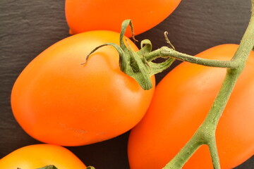 Several organic yellow plum tomatoes on a slate board, close-up, top view.