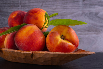 juicy and ripe peaches lie in a carved wooden plate