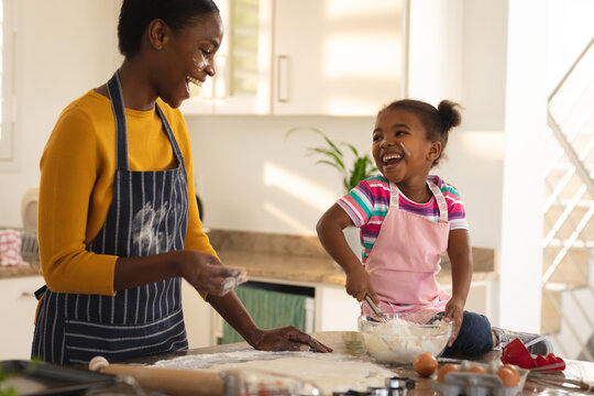 Laughing african american mother and daughter baking in kitchen making dough together