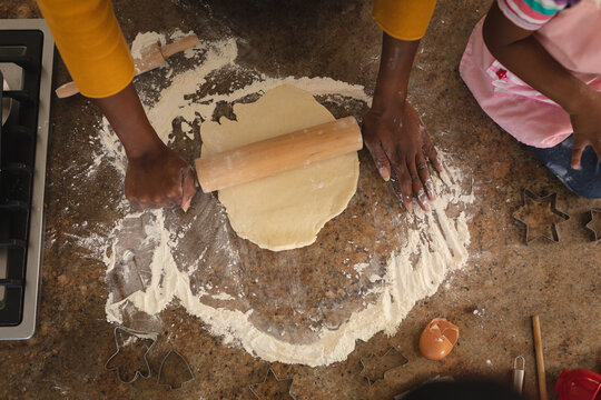 High angle of african american mother and daughter baking in kitchen rolling dough together