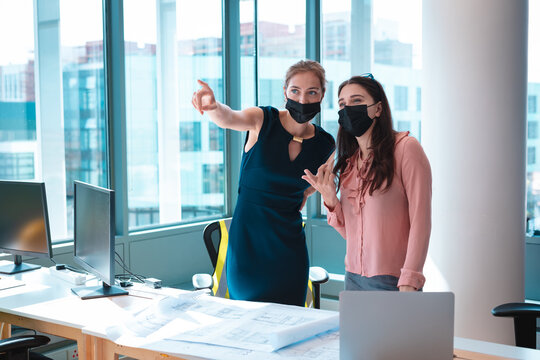 Two caucasian businesswomen wearing face mask and discussing