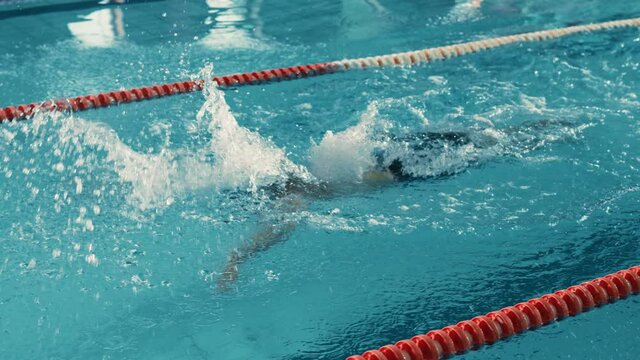 Successful Male Swimmer Racing, Swimming in Olympic Swimming Pool. Professional Athlete Determined to Win Championship using Butterfly Style. Colorful Cinematic Shot. Side View Tracking Slow Motion