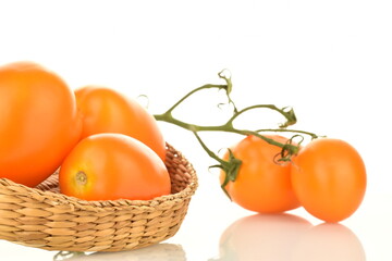 Several appetizing yellow plum tomatoes with a straw plate, close-up, isolated on white.