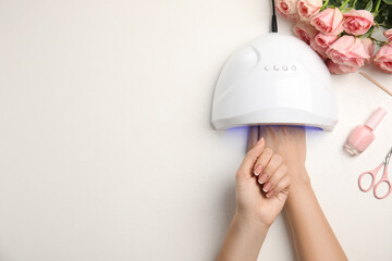 Woman using ultraviolet lamp to dry gel nail polish at white table, top view. Space for text
