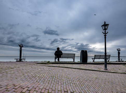 Een man in silhouet  zit alleen op een bankje in Volendam starrend over het bevroren  Markermeer