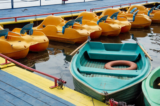Rowboats and pedal boats are tied to the pier. There is a lifebuoy inside the boat. Pier on the lake. Yellow pedal boats at the pier.