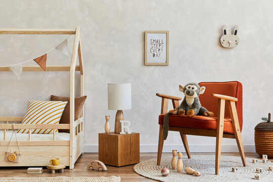 Stylish composition of cozy scandinavian child's room interior with bed, red armchair, plush and wooden toys and textile hanging decorations. Creative wall, carpet on the floor. Copy space. Template.