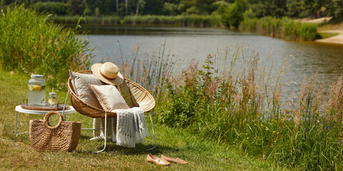 Stylish composition of outdoor garden on the lake with design rattan armchair, coffee table, plaid,...
