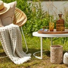 Stylish composition of outdoor garden on the lake with design rattan armchair, coffee table, plaid, pillows, drinks and elegant accessories. Summer chillout mood.