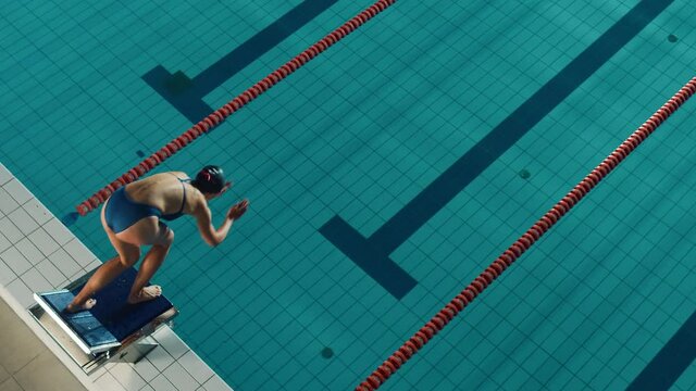 Beautiful Female Swimmer Diving in Swimming Pool. Professional Athlete Gracefully Jumps. Person Determined to Win Championship. Cinematic Static Lock Shot. Slow Motion, Stylish Colors, Artistic Aerial