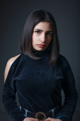 Portrait of serious beautiful young woman with black hair on gray background. Studio shoot, fashion concept.
