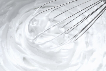 Whipping white cream with balloon whisk, closeup view