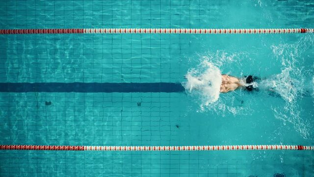 Aerial Top View: Muscular Male Swimmer in Swimming Pool. Professional Athlete Swims in Butterfly Style, Determination in Training to Win Championship. Cinematic Slow Motion, Stylish Colors